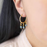 Image shows model wearing gold Triple Birthstone Huggie Hoop Earrings with March birthstone  Edit alt text