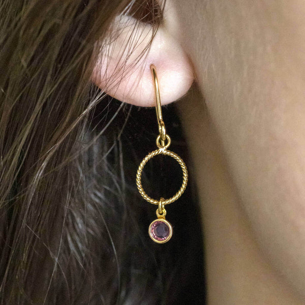 Image shows model wearing twisted gold circle mini birthstone earrings