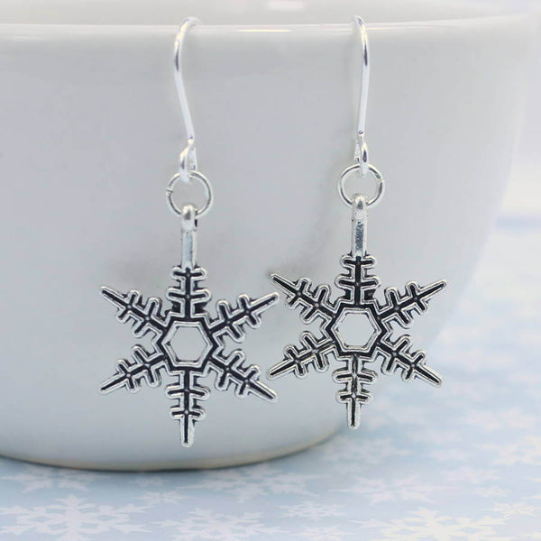 Image shows vintage style snowflake earrings hanging from a whit bowl