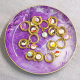 Image shows a selection of enamel ying and yang huggie hoop earrings in a purple trinket dish