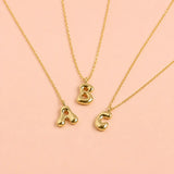 Personalised gold bubble initial necklaces with A B and C letter pendants on a pale pink background
