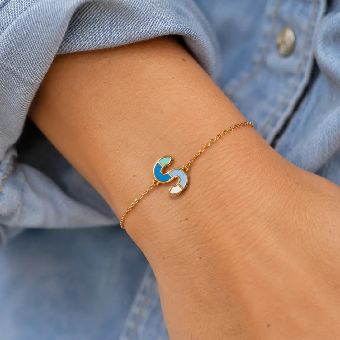 Personalised gold plated enamel initial bracelet with blue S letter charm worn on the wrist
