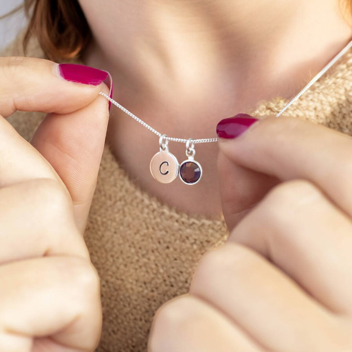 a steling silver personalised birthstone necklace is worn by a woman in a beige knitted top