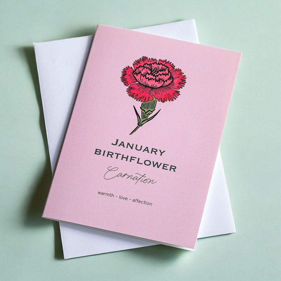 Pink greeting card with a hand-drawn carnation illustration and “January Birthflower” text, placed on a soft green background with a white envelope.