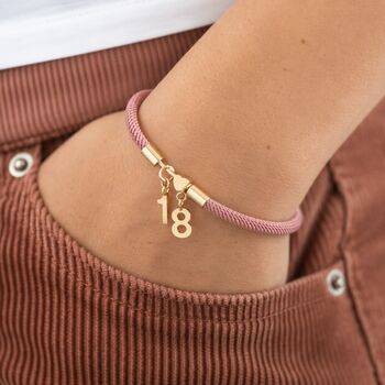 Pink cord bracelet with gold heart detail and number 18 charm, styled as a colourful everyday birthday accessory
