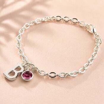 Silver charm bracelet with an initial pendant and pink birthstone crystal, minimalist personalised jewellery.
