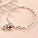 Silver charm bracelet with an initial pendant and pink birthstone crystal, minimalist personalised jewellery.

