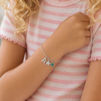 Silver children's bracelet worn with letter charm, star pendant and bright blue birthstone