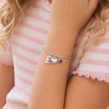 Silver children's charm bracelet styled with an initial letter, heart charm and purple birthstone