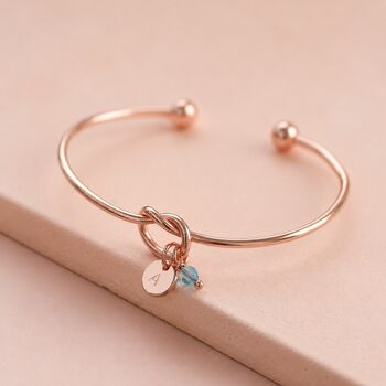 Rose gold knot bangle with personalised initial disc and blue crystal charm, perfect for layering with bangles.