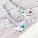 Silver charm bracelets layered with initial discs, birthday number charms and crystal birthstones