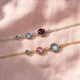 Silver and gold birthstone bracelets on pink fabric, featuring three colourful crystal stone settings