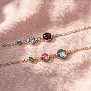 Silver and gold birthstone bracelets on pink fabric, featuring three colourful crystal stone settings