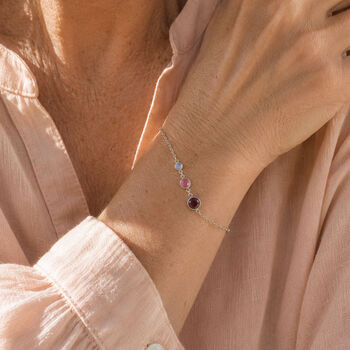 Silver birthstone bracelet styled with a pink blouse, featuring three colourful crystal birthstones