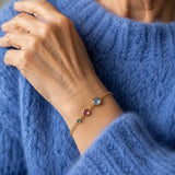 Gold birthstone bracelet styled with a blue jumper, showcasing three colourful crystal birthstones