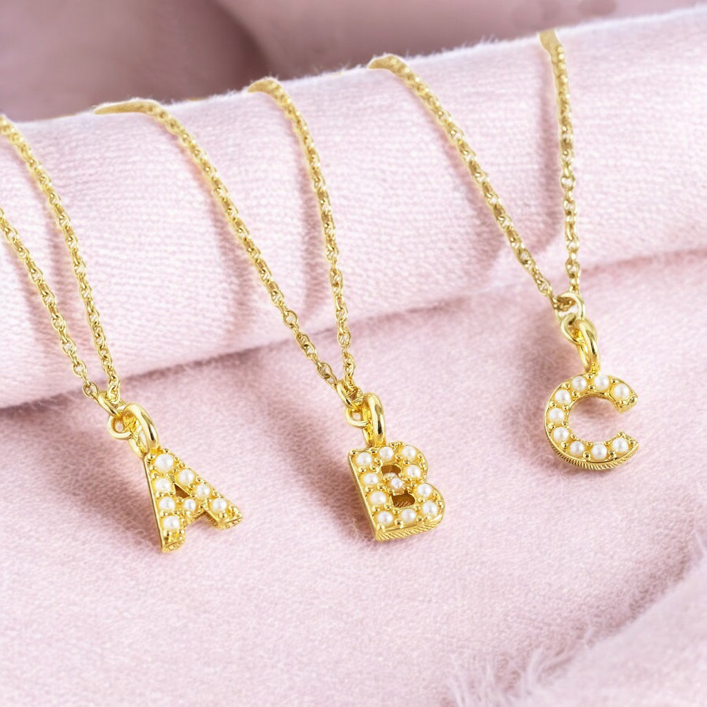 image shows three gold plated dainty pearl initial necklaces A B and C on a pink background