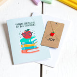 Close-up of A+ Teacher card and apple necklace displayed together on a desk