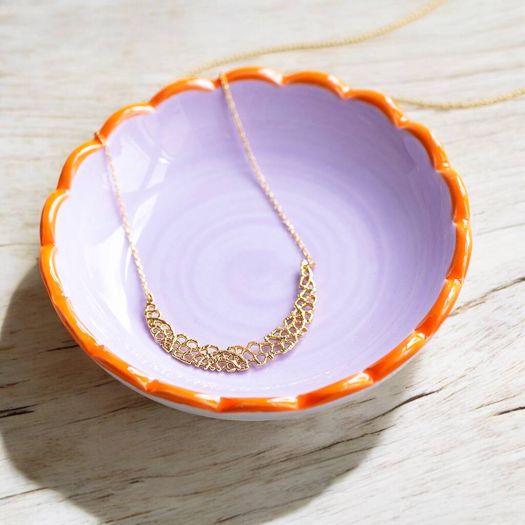 Gold crescent moon charm necklace presented on a purple jewellery round dish.