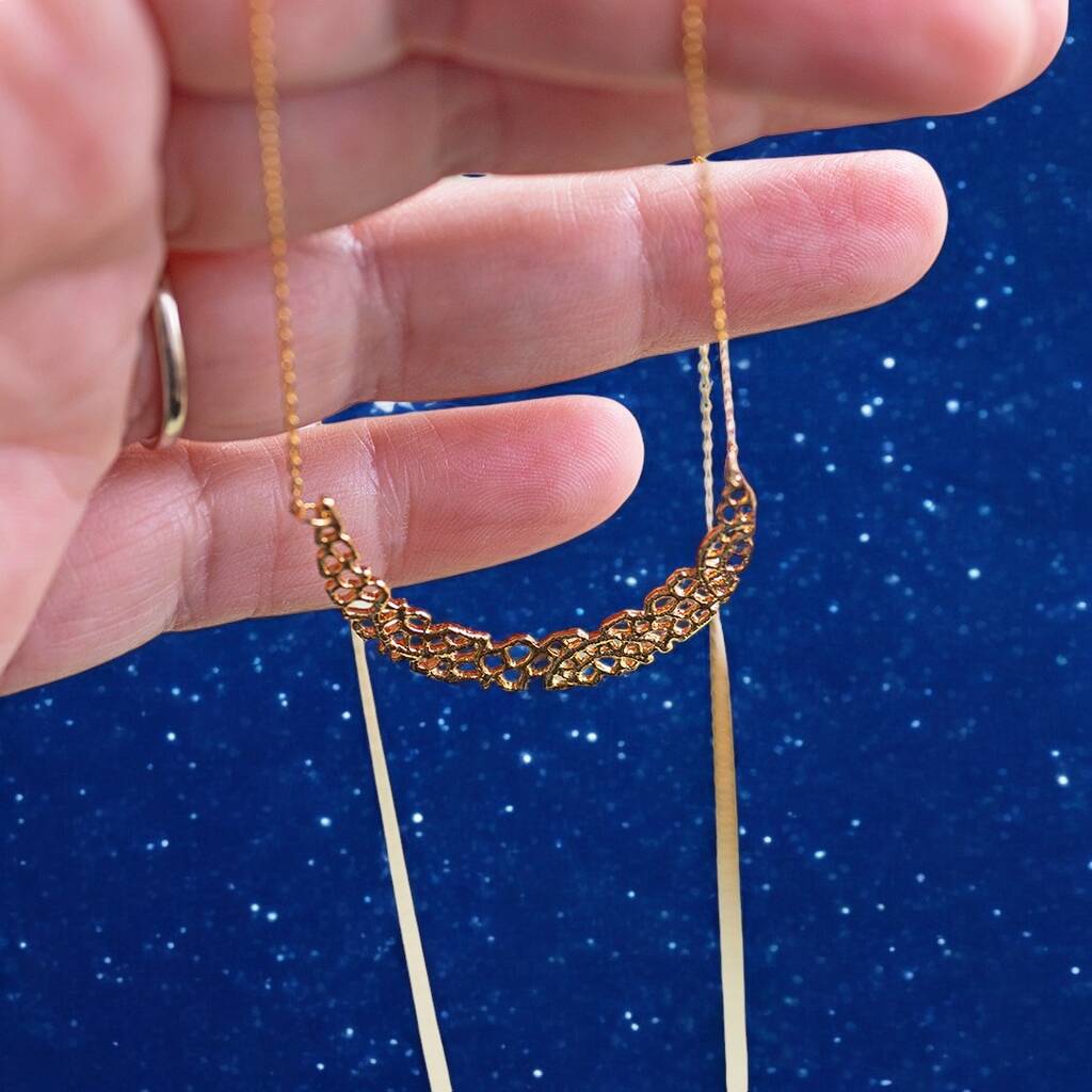 Long length gold crescent moon charm necklace being held in a women's hand.