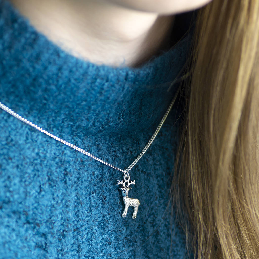 image shows a silver plated reindeer necklace worn by a woman in a teal chunky knit jumper