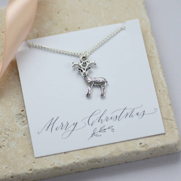 image shows a silver plated reindeer necklace presented on a Merry Christmas sentiment card on a natural tile background