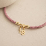 Gold number 18 charm bracelet with a pink woven cord and heart detail, perfect for layering with everyday jewellery