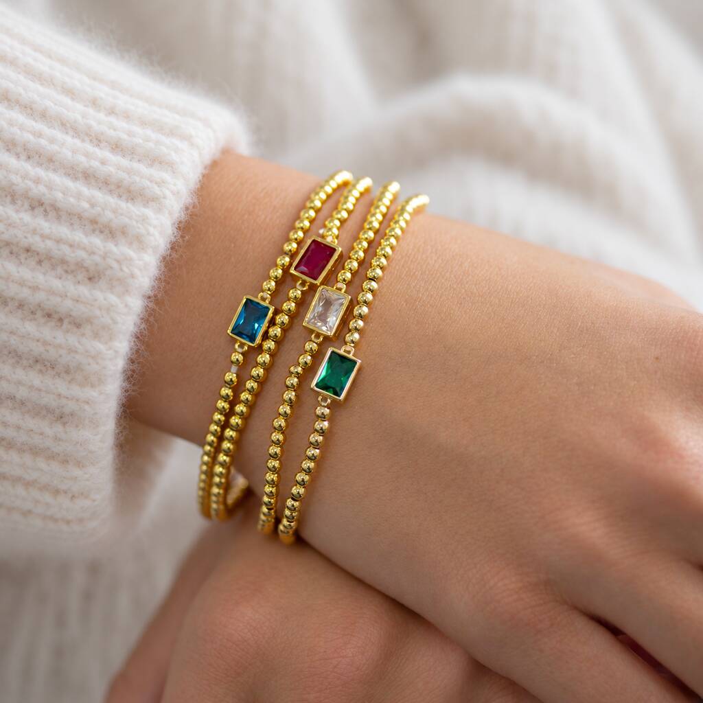 Stack of four gold beaded birthstone bracelets with colourful baguette stones worn together on wrist.