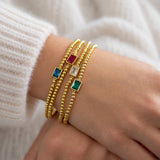 Stack of four gold beaded birthstone bracelets with colourful baguette stones worn together on wrist.