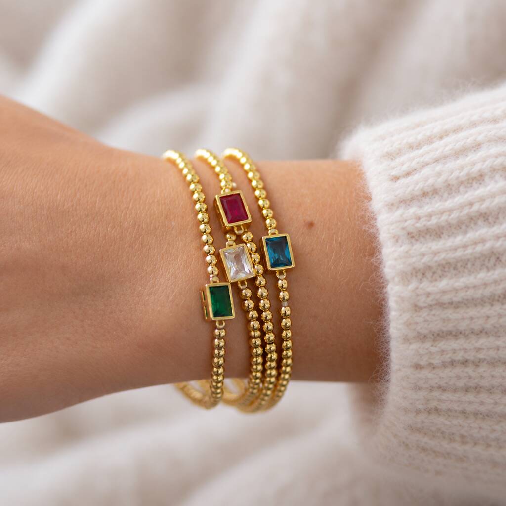 Gold beaded birthstone bracelets stacked on wrist with colourful baguette-cut stones representing loved ones.