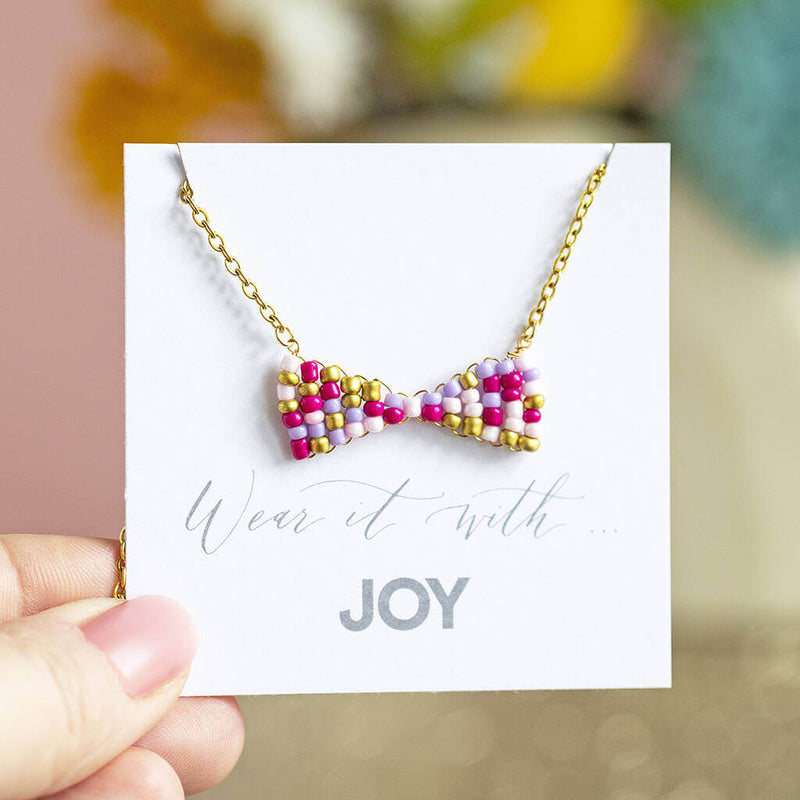 Image shows gold plated Beaded Bow Necklace on a 'Wear it with JOY' sentiment card.