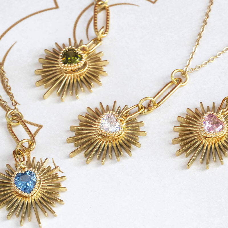 Image shows three Birthstone Heart Starburst Necklaces on a white backdrop. From left to right: September Sapphire, August Peridot, April Crystal and October Rose.