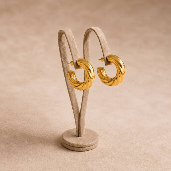 Bold Twisted Gold Hoop Earrings showcased on a display stand, featuring a sculptural twisted design and glossy finish