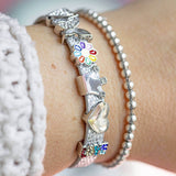 Silver faux leather buckle bracelet with sparkly heart, sparkly butterfly, enamel coloured flower, shiny crown, shiny heart and sparkly LOVE charms worn on a wrist. Bracelet fully adjustable and suitable for a child or adult wrist.