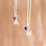 Image shows two Child's Silver Plated Initial and Birthstone Necklaces from left, letter "A" with pink birthstone and letter "H" with September birthstone.