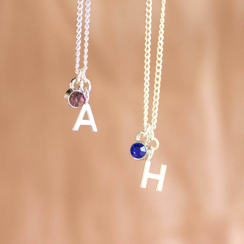 Image shows two Child's Silver Plated Initial and Birthstone Necklaces from left, letter "A" with pink birthstone and letter "H" with September birthstone.