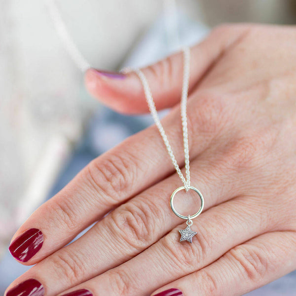 Image shows a silver circle pendant with hanging crystal sparkle star charm laid over a hand.