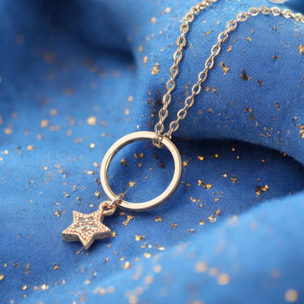 Image shows a gold circle pendant with hanging crystal star charm on a blue background.