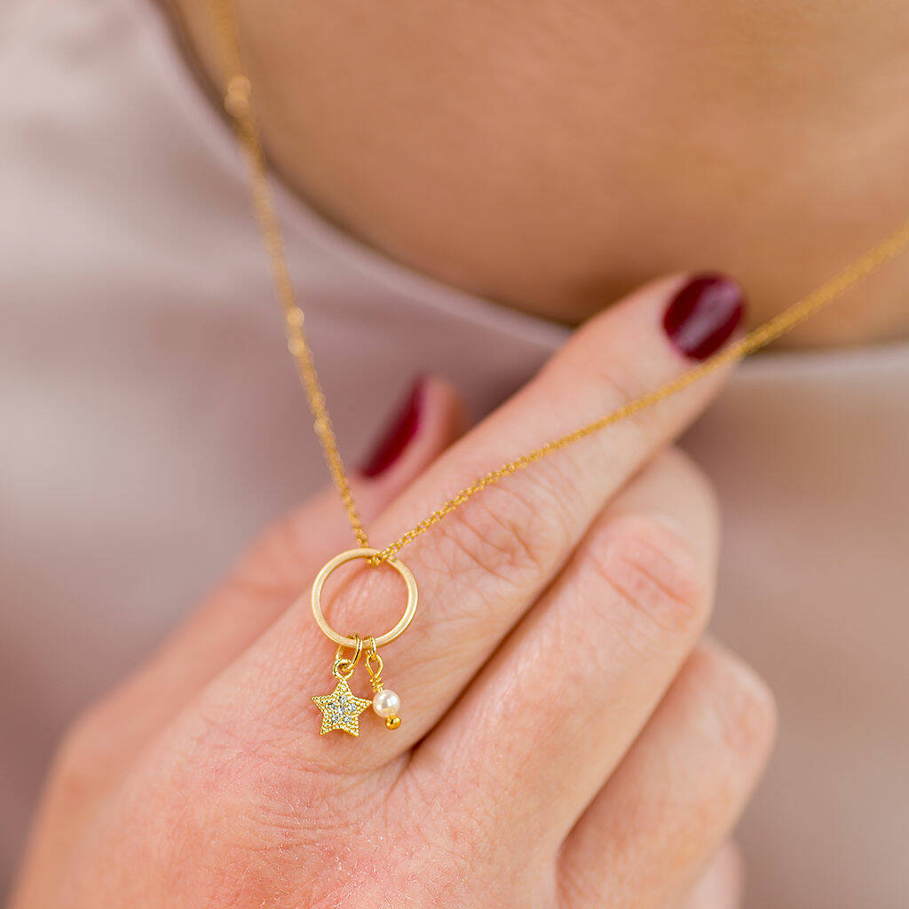 Image shows a gold circle pendant with hanging crystal star charm worn over a pale pink top.