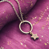 Image shows a gold circle pendant with hanging crystal star charm on a burgundy background.