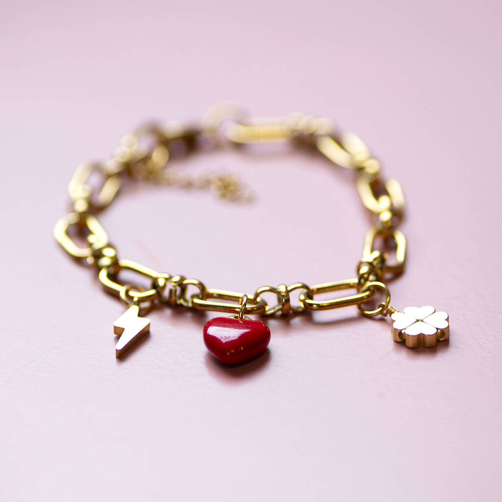 Personalised gold charm bracelet with chunky chain featuring red heart, lightning bolt and clover charms on pink background