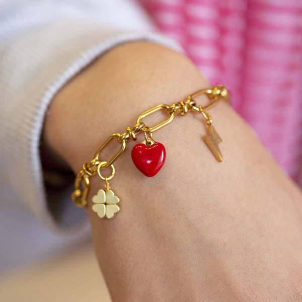 Chunky gold charm bracelet worn on wrist with red heart, clover and lightning bolt charms as personalised jewellery