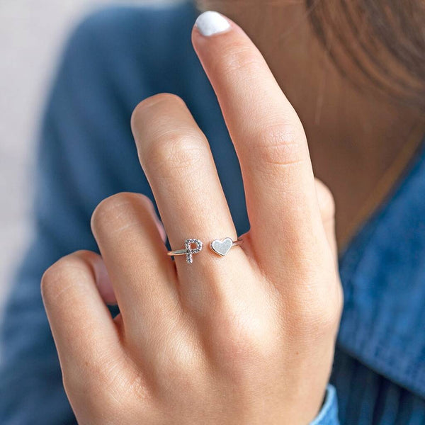 A silver plated ring with crystal encrusted initial charm and a heart charm worn on the middle finger.