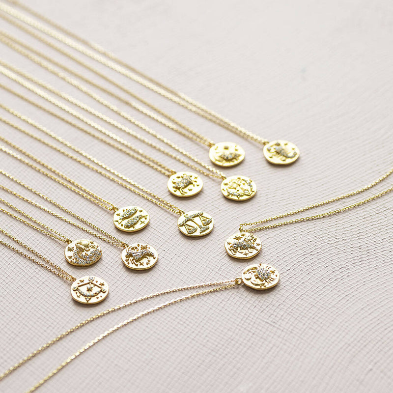 Image shows Crystal Zodiac Coin Necklaces on a plain backdrop.