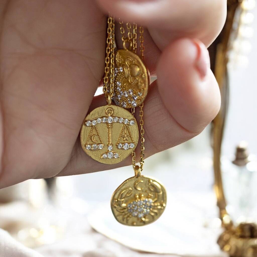 image shows three of the twelve crystal zodiac coin necklaces displayed on a woman's hand 