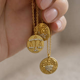 Close-up of gold zodiac coin necklaces with crystal-embellished Libra and Cancer charms on fine chains