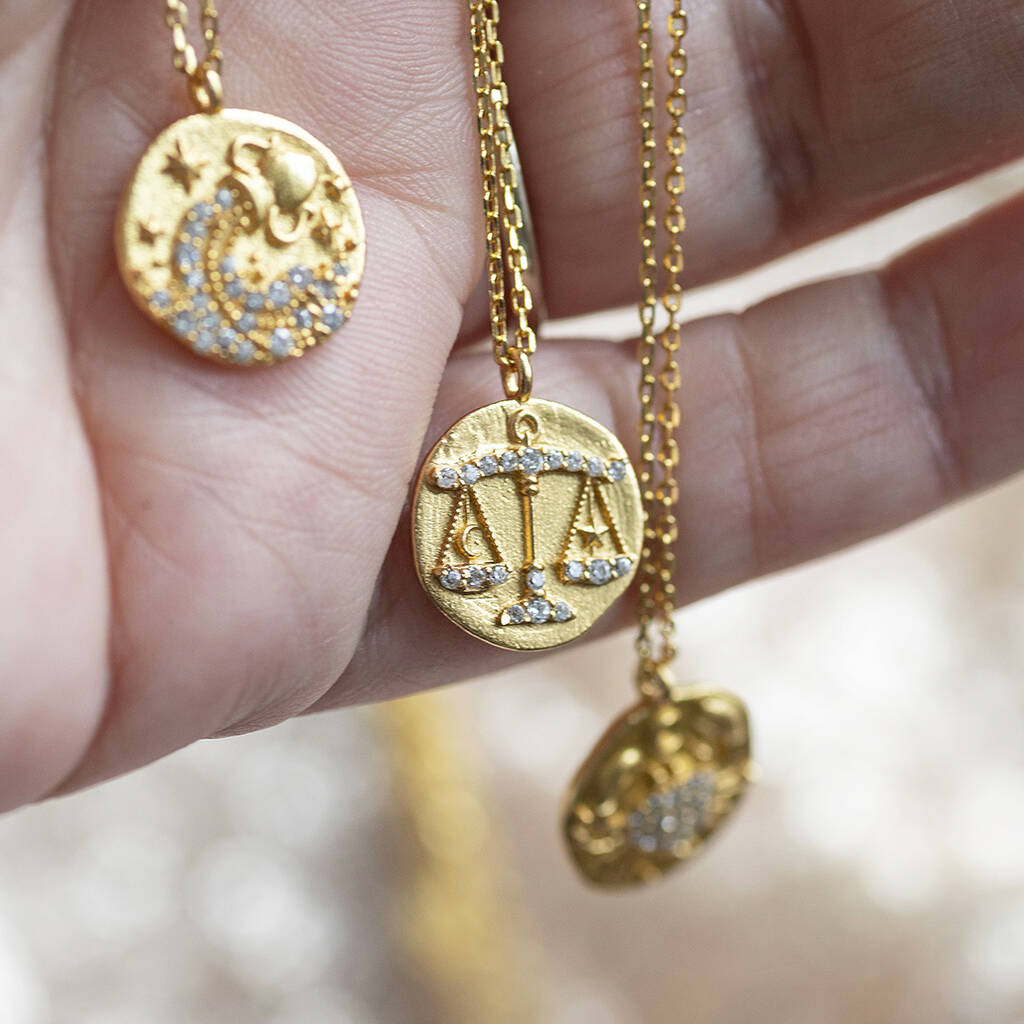 image shows three of the twelve crystal zodiac coin necklaces displayed on a woman's hand 