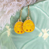 yellow chick enamel Easter egg charms on gold plated earring hooks displayed on a green plant pot