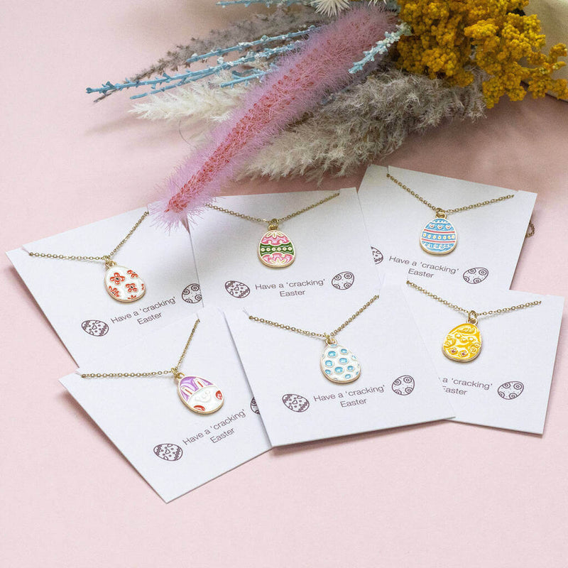 six designs of enamel easter egg charm gold plated necklaces displayed on a 'Have a 'cracking'Easter sentiment card. Flat image.