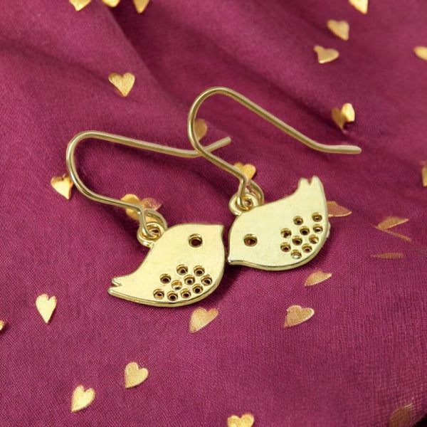 image shows a pair of gold love bird earrings on a maroon fabric background with gold heart detail