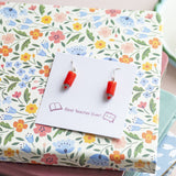 Red pencil drop earrings on a floral gift display, colourful statement jewellery with silver hooks.